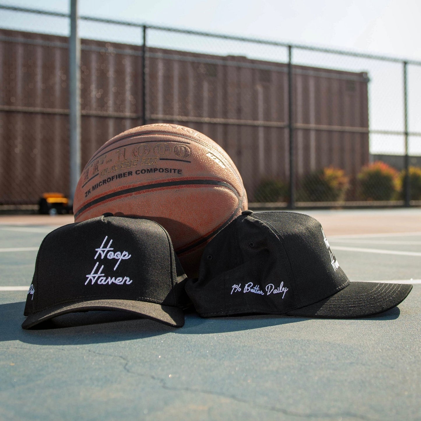 Two Black Hats on a basketball court. The hats have white text on them that say "Hoop Haven" in a cursive font.